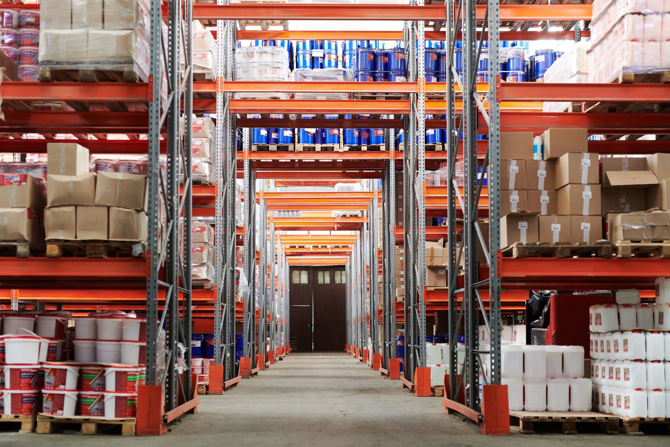 Warehouse pallet racks stocked with cartons beside a wide concrete aisle.